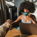 a woman in front of the laptop petting a dog
