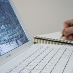 Person writing near a lap top