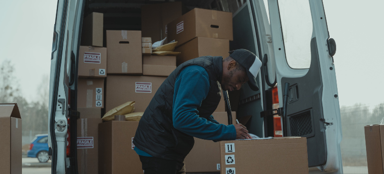 a person filling out a form in front of a van full of cardboard boxes