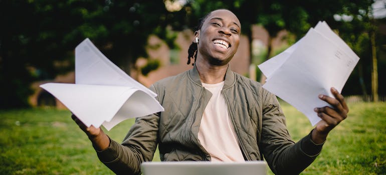 a man with a smile on his face holds papers while working on his laptop