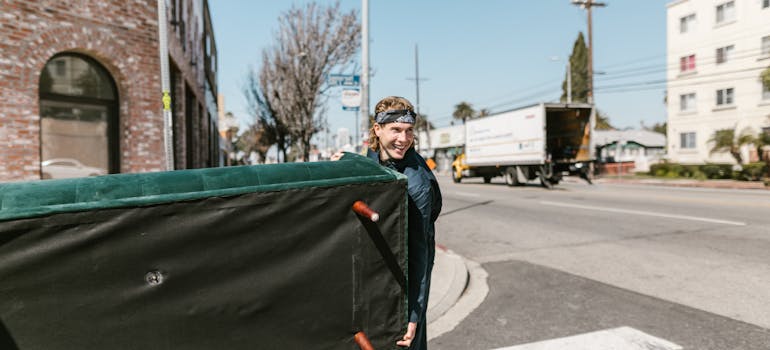 a professional mover carrying a green, velvet sofa across the street